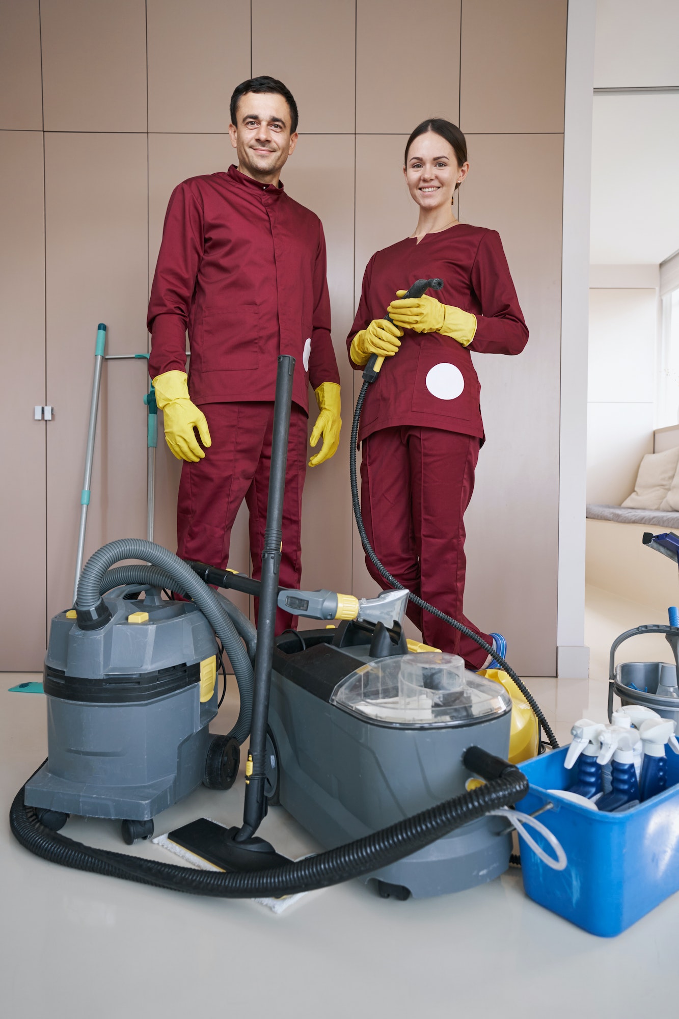 Cheerful housecleaners with cleaning equipment standing in room